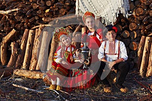 Three adorable kids in folk Russian costume and headdresses with samovar and in ancient shoes
