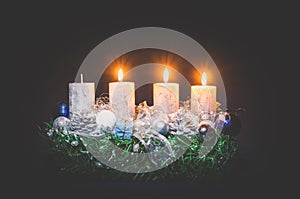 Three advent candles burning on black background