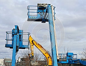 Three aerial working platforms of cherry picker and an excavator boom in an industrial area