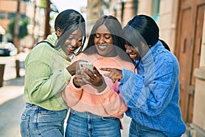 Three african american friends smiling happy using smartphone at the city