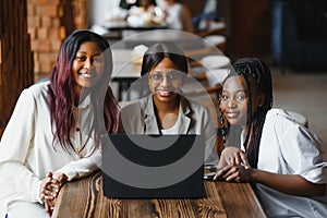 Three African American girls students sitting at the table in cafe studying up for test or making homework together, they are