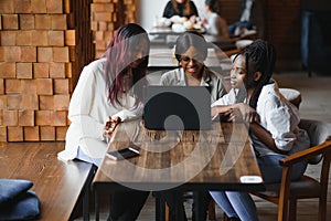 Three African American girls students sitting at the table in cafe studying up for test or making homework together, they are