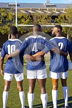 Three African American young male athletes in blue jerseys, white shorts on field outdoors