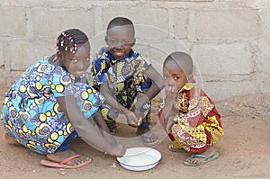 Three African Children Sitting Outdoors Eating Rice in Africa