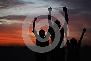 Three African Siblings Raising Their Hands Against A Colorful Evening Sky