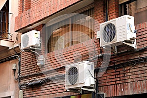 Three air conditioning units on the outside red brick wall of a