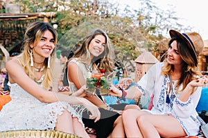 Three amazing girls in stylish vintage clothes having fun in outdoor cafe and drinking cocktails. Group of friends