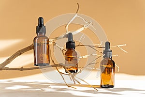 Three amber glass bottles with dropper lid on beige background in rays of sunlight. Serum for face close-up among