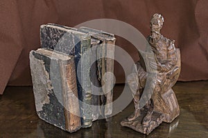 Three ancient stained books by a statue of a philosopher