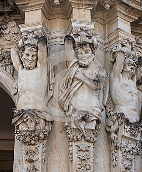 Three ancient statues of satyrs holding something