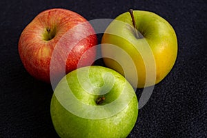 Three apples, one green and two red and yellow on a dark background