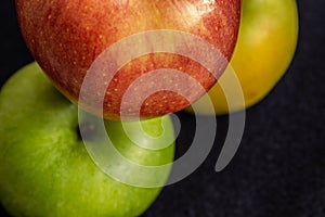 Three apples, one green and two red and yellow on a dark background