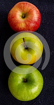 Three apples, one green and two red and yellow on a dark background