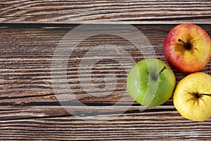 Three apples (red, green, and yellow) on wooden table, top view, copy space