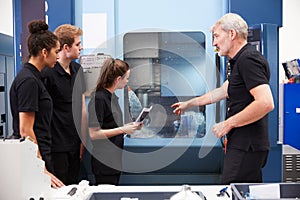 Three Apprentices Working With Engineer On CNC Machinery