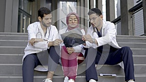 Three Arabian doctors interns, sitting outdoor on clinic stairs and discussing skull x-ray