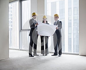 Three architects in hardhats examining a blueprint in an office building