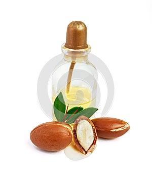 Three argan nuts with green leaves glass bottles on isolated white background. Chopped argan nut with a drop of oil