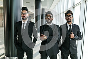 Three asian business people with arms crossed standing near the window in conference room