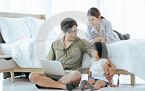 Three Asian family members consist father, mother, little daughter helping or supporting the girl doing homework, using laptop in