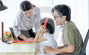 Three Asian family members consist father, mother, little daughter wearing headphones, helping or supporting girl using laptop in