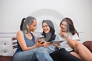 three Asian girls joke while using a cell phone and a tablet