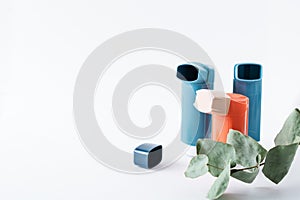 Three asthma inhalers and a eucalyptus branch on an isolated white background. Medical concept