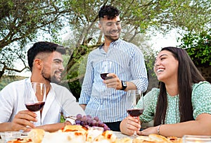 Three attractive young happy people celebrating outdoor holding red wine glasses - Stylish millennial friends having fun in the