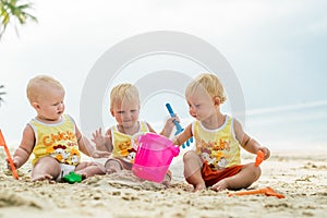 Three baby Toddler sitting on a tropical beach in Thailand and playing with sand toys. The yellow shirts. Two boys and one girl