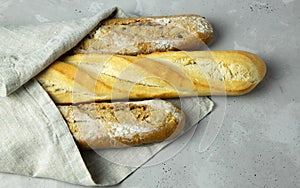 Three baguettes on a brown linen napkin lie on a gray concrete background. Bread. Bakery