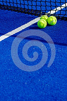 Three balls near the net of a blue padel tennis court, racket sports concept