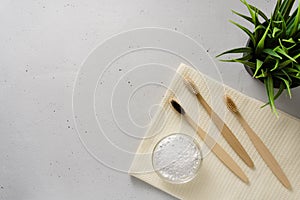 Three bamboo toothbrushes, tooth powder and towel on a light gray concrete background.