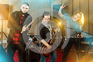 Three bandmates posing together with musical instruments in rehe