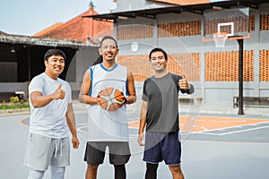 three basketball players smiling while carrying basketball and thumbs up