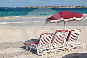 Three beach loungers and umbrella on sand