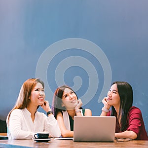 Three beautiful Asian girls looking upward to copy space while working at cafe