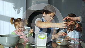 Three beautiful children cook baking in the kitchen, break the egg into flour, pour water and knead the dough