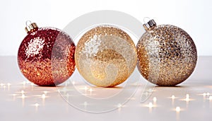 Three beautiful Christmas ornaments in red, gold, and silver with a white background and twinkling lights