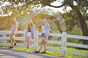 Three beautiful girl standing on fence outdoor warm tone.