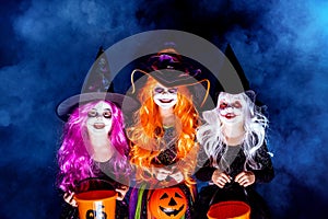 Three Beautiful girl in a witch costume on a dark background in smoke scaring and making faces