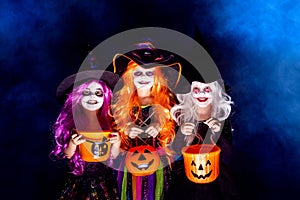 Three Beautiful girl in a witch costume on a dark background in smoke scaring and making faces