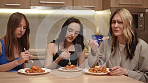 Three beautiful girls are sitting in the kitchen at a table with food on plates and eating. Not all girls like what they