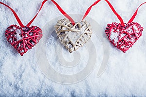 Three beautiful romantic vintage hearts are hanging on a red band on a white snow background. Love and St. Valentines Day concept.