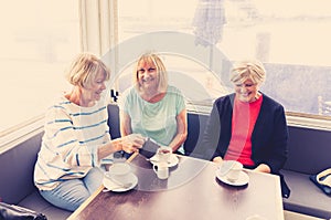 Three beautiful senior women enjoying retirement together having tea or coffee