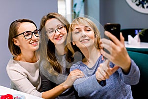 Three beautiful young women enjoying coffee and cake together in a cafe sitting at a table laughing and making selfie