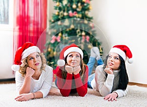 Three beautiful young women lying in front of a Christmas tree