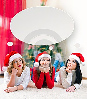 Three beautiful young women lying in front of a Christmas tree