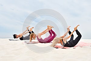 Three beautiful young women perform Dhanurasana yoga pose