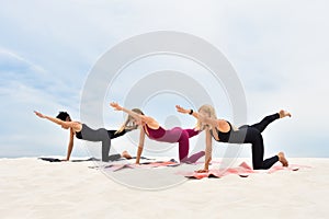 Three beautiful young women perform yoga exercises