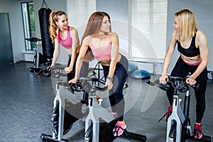 Three beautiful young women working out on bikes at the gym.